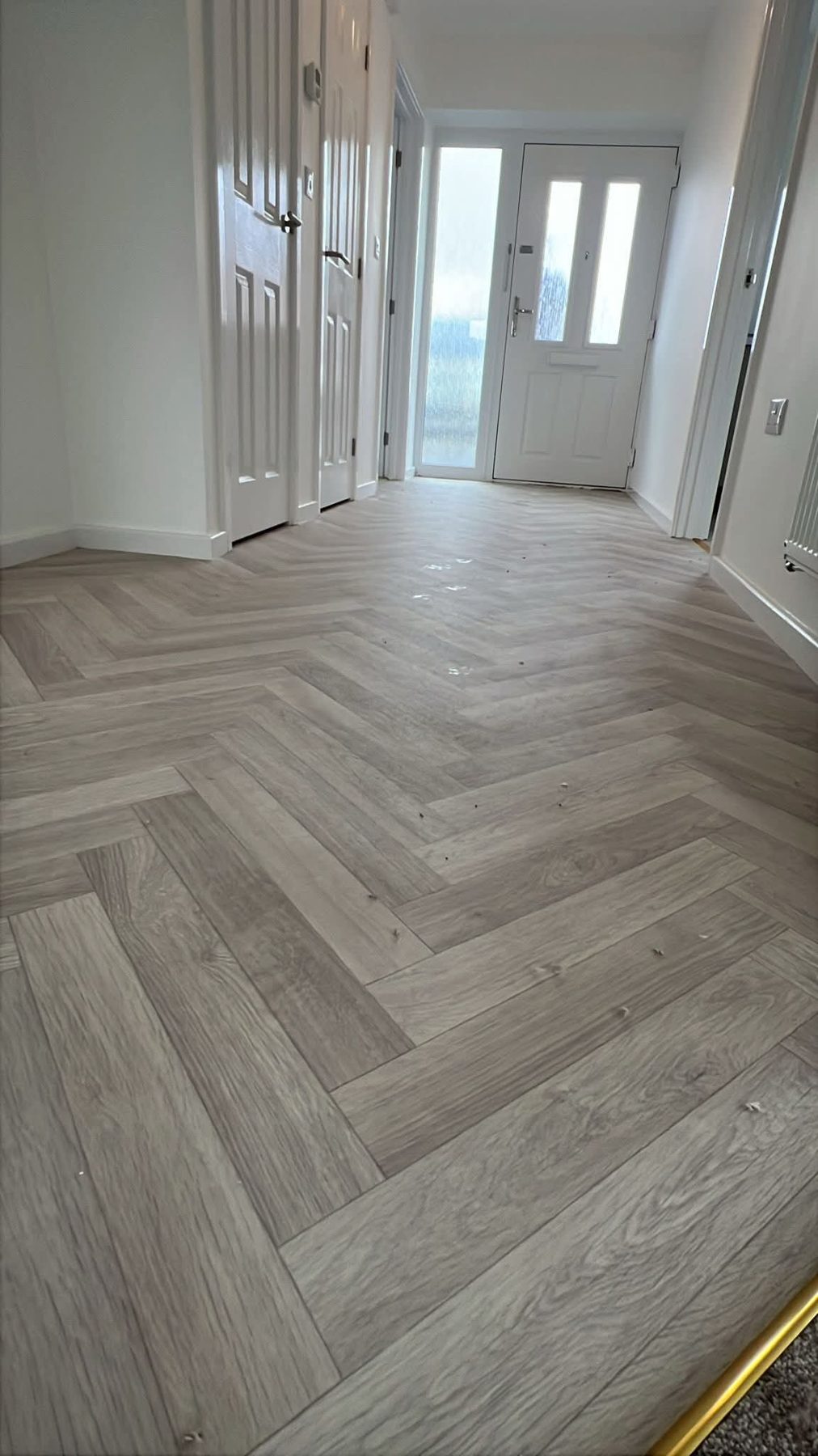 Grey herringbone floor laid down a hallway to a white front door