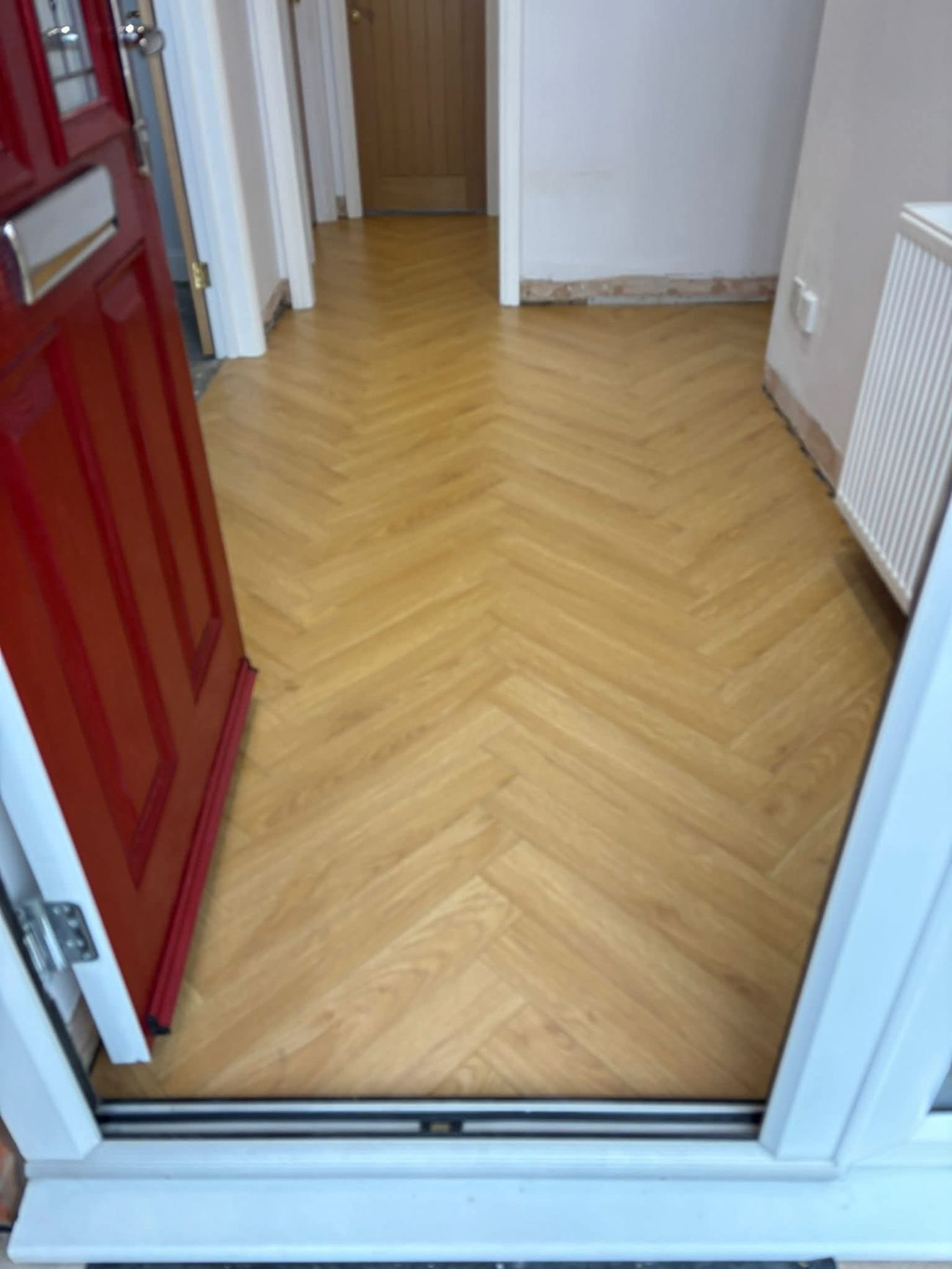 Warm oak herringbone floor in a hallway beside a red front door