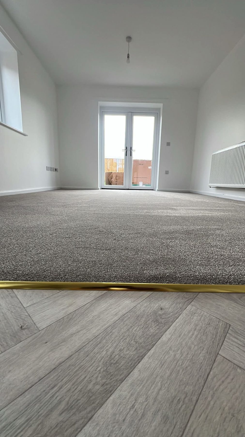Grey carpet meeting herringbone flooring at a brass threshold strip